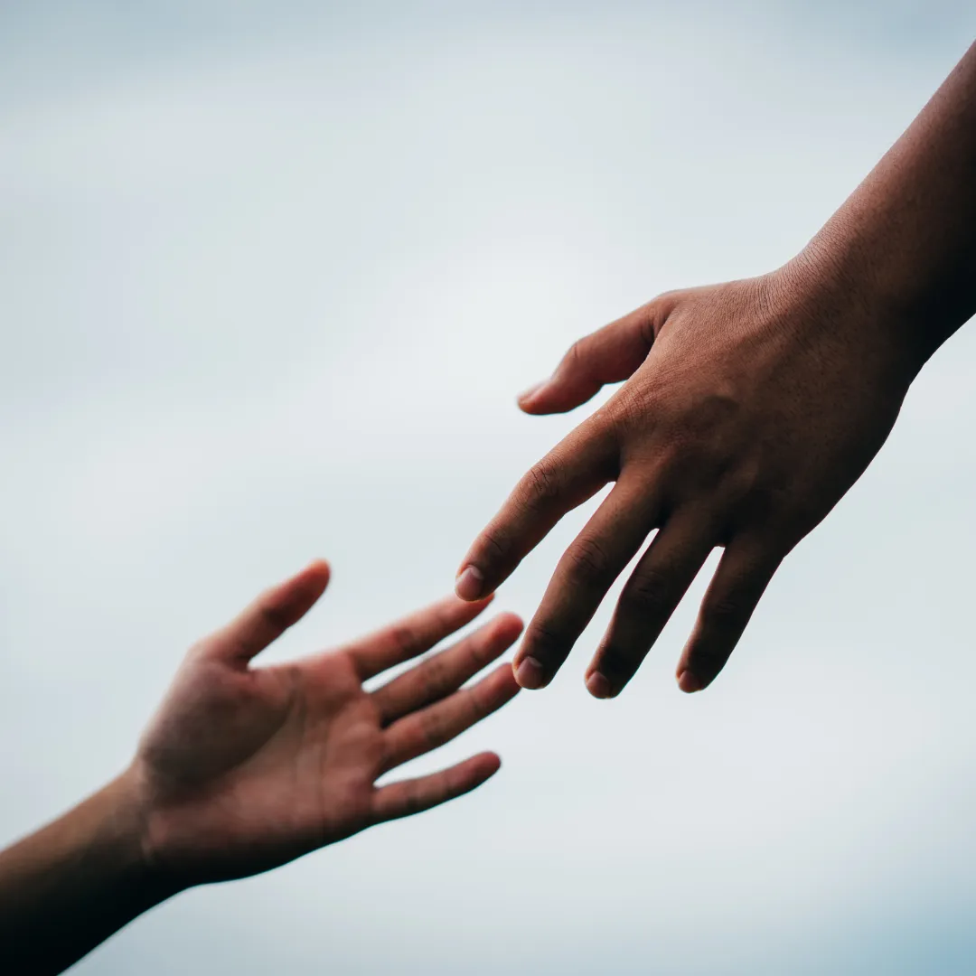 Two hands reaching toward each other against a soft sky
