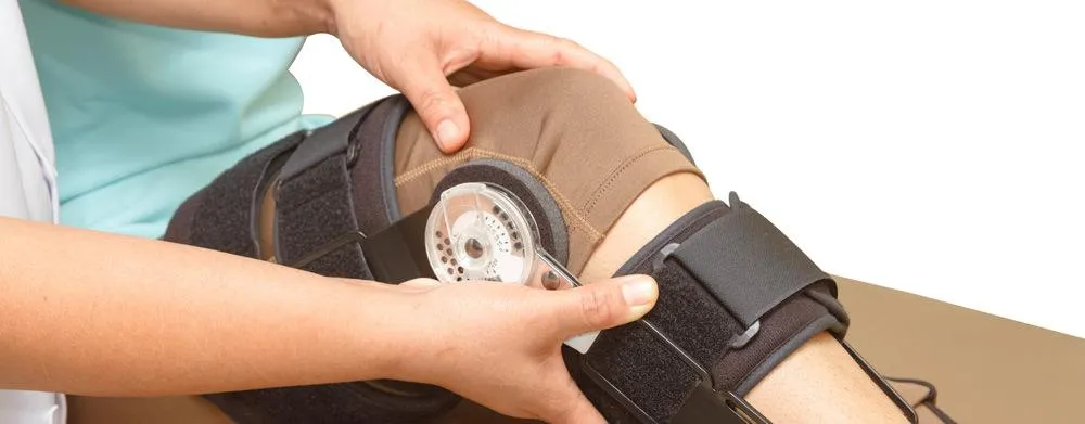 A clinician adjusts a hinged range-of-motion knee brace on a patient's leg