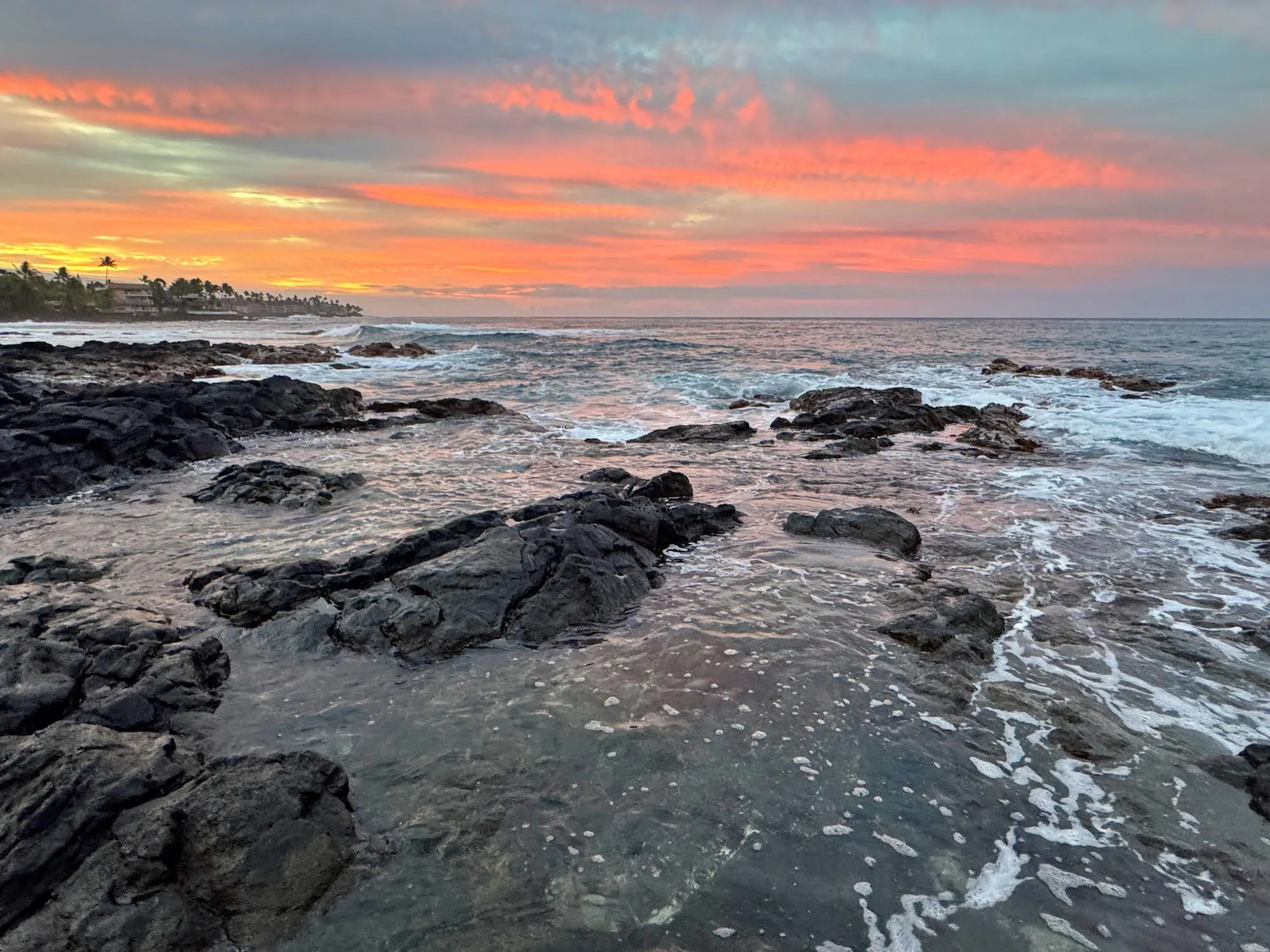 The sun setting over a lava-rock shoreline on the Kona coast