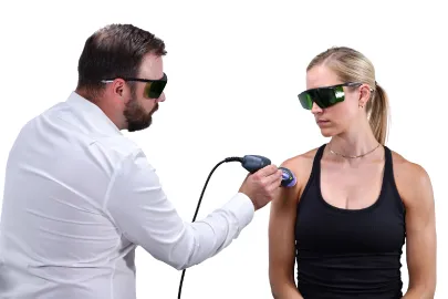 A clinician applies a handheld MLS laser to a patient's shoulder; both wear protective glasses