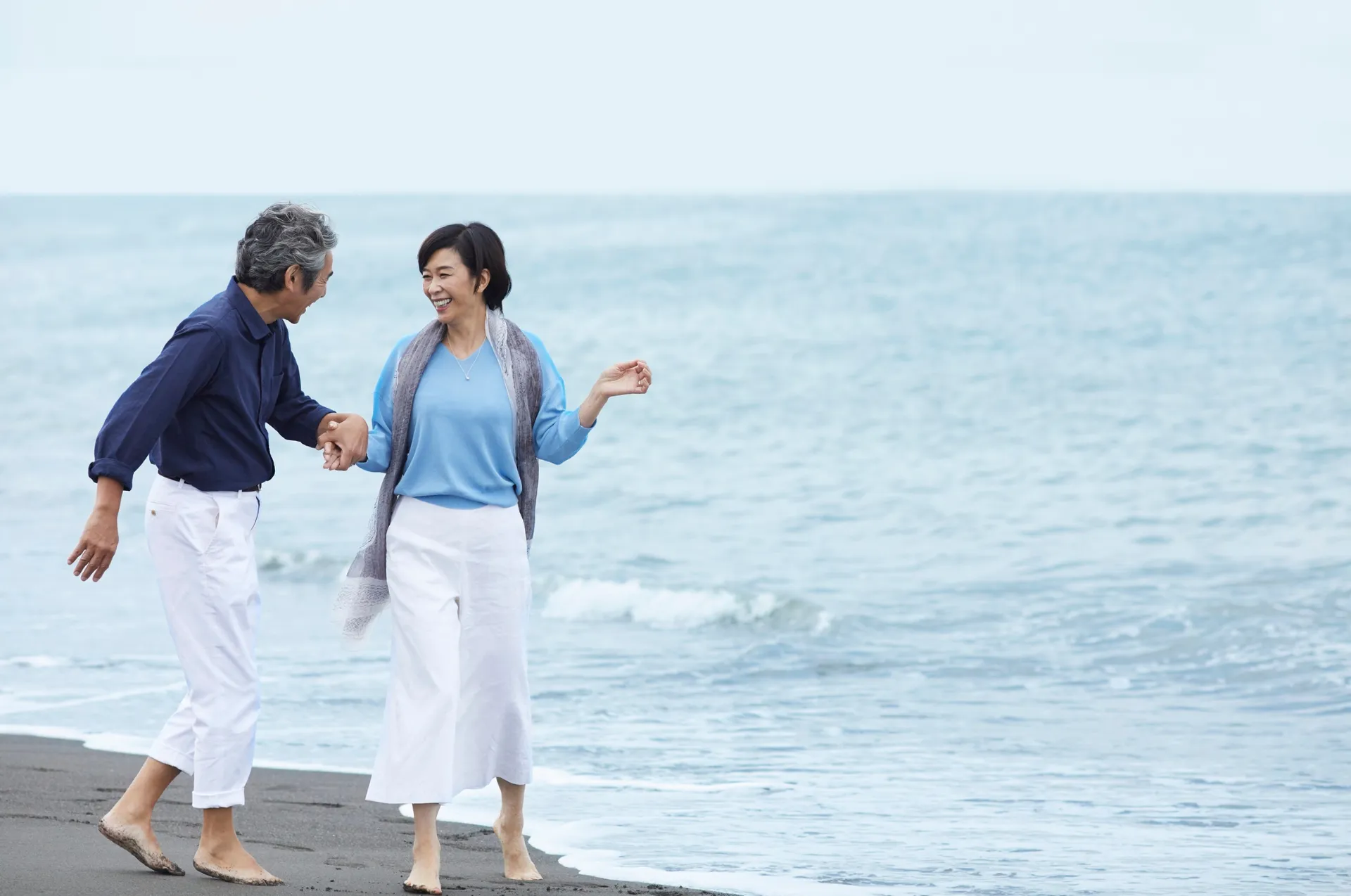 An older couple laughs together while walking along a Hawaiian beach