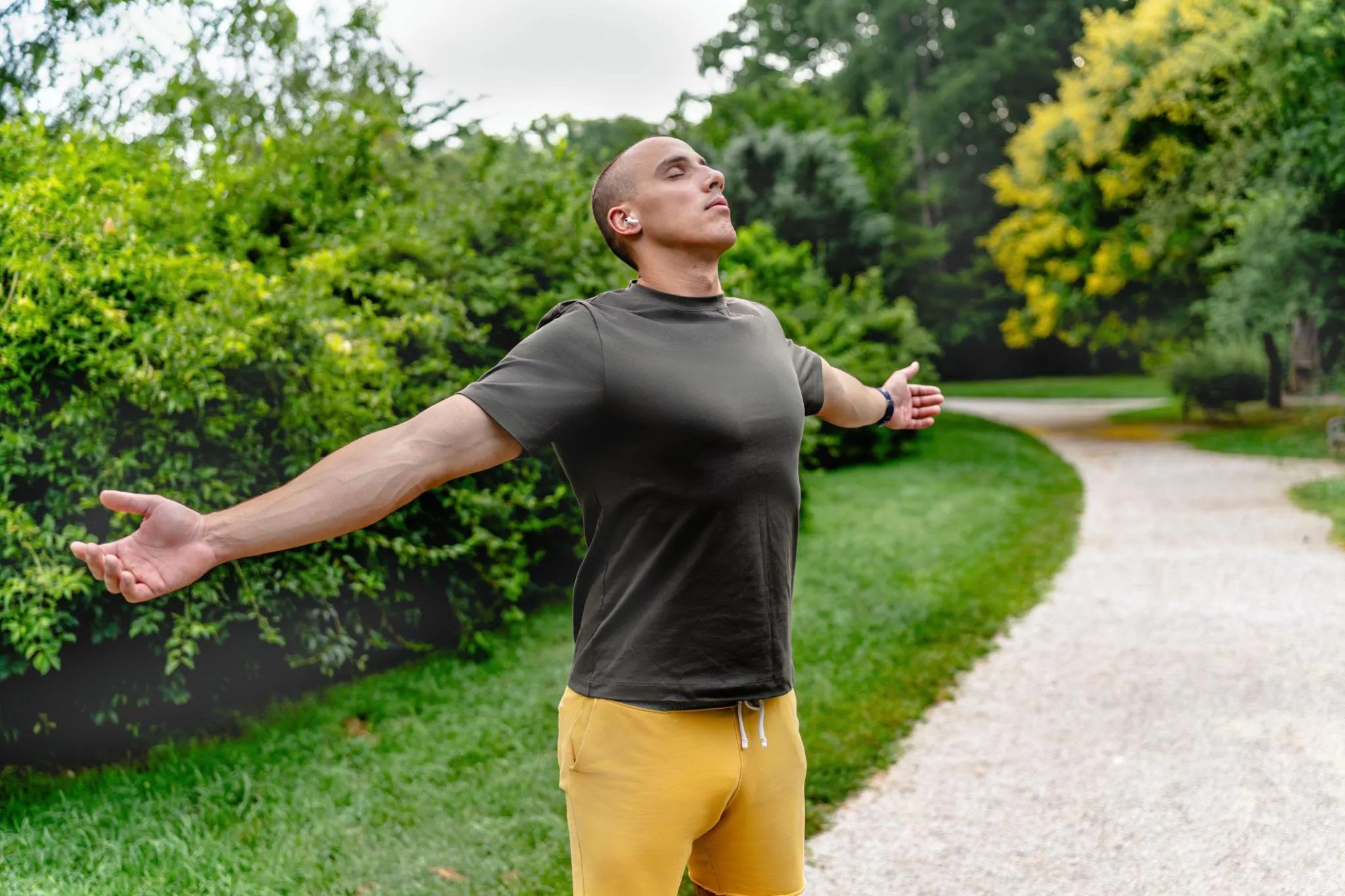 A man pauses to breathe deeply on a tree-lined park path